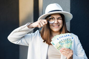 Attractive woman with cash in her hands and magnifying glass. Woman examines banknotes in her hands