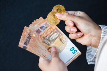 Closeup womans hands holding gold coins of crypto currency and euro banknotes, wearing in white jacket. The concept of cash payments, savings and salaries