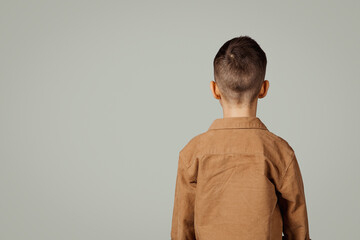 Small european child in shirt isolated on gray background, back with copy space, unrecognizable