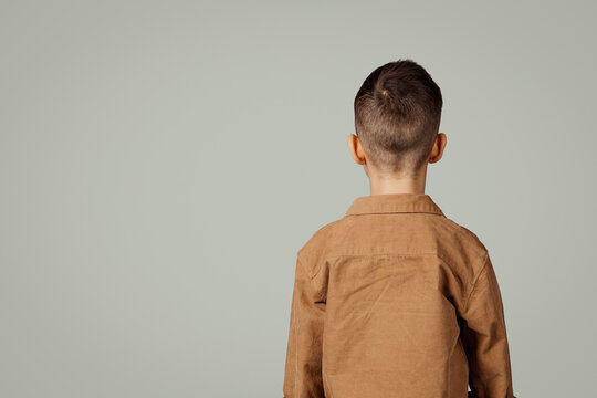 Small european child in shirt isolated on gray background, back with copy space, unrecognizable