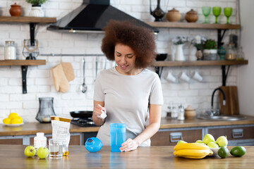 Young sporty african american woman pouring protein powder into a cup to make replacement food meal after workout