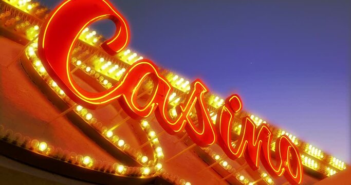 A low angle establishing shot of a flashing neon Casino sign at night.  	