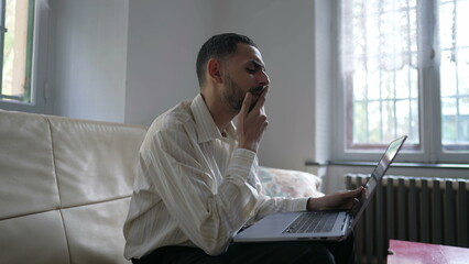 One concentrated Arab young man reading content online in front of laptop at home. A focused Middle Eastern person with computer on lap staring at screen