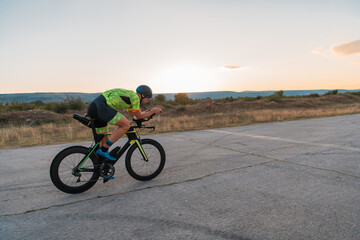  Triathlete riding his bicycle during sunset, preparing for a marathon. The warm colors of the sky provide a beautiful backdrop for his determined and focused effort.