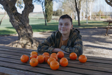 a boy sits in the garden at a wooden table with oranges