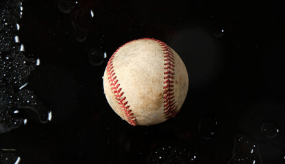 Used ball from baseball sport in water on black background, rain game concept.