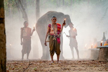 Mahout teacher hold torch and stand in front of other mahout and elephant in concept of traditional ceremony.