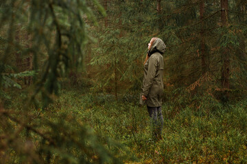 Woman in Green Raincoat Looking into the Dark Forest in the Rain
