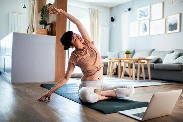 Young Japanese woman doing yoga while using a laptop