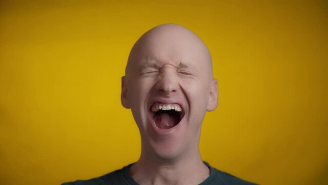 Man with blue eyes and bright skin looking straight towards the camera and makes a big yawn on a yellow background, Real time.