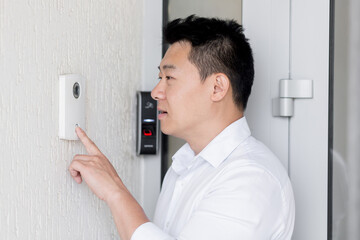 An Asian man stands at the door of a house, office, hotel and presses the door bell of an automatic...