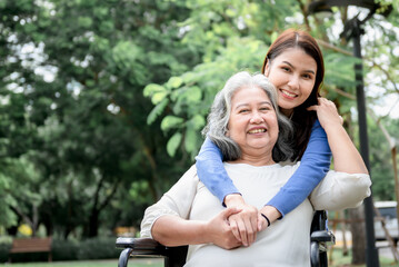 Naklejka premium Asian family, attractive daughter looking and taking care her mother is patient with paralysis, Sitting on a wheelchair, at green garden, to relationship in family and health care concept