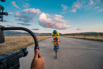 Fototapeta na wymiar A videographer recording a triathlete riding his bike preparing for an upcoming marathon.Athlete's physical endurance and the dedication required to succeed in the sport.