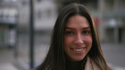 Obraz premium Portrait of a happy young brunette woman smiling at camera standing in urban city street. Confident adult girl in 20s close up face in cinematic tracking shot