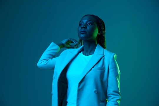African american woman portrait business smile and fashion wearing glasses on blue background in neon light, color mixed light, bright color dancing, futuristic party. Flying pigtails hair emotions.