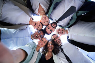 Multiethnic group of work colleagues embraced in circle, face down taking a selfie smiling and...