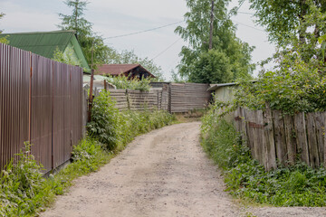 unpaved dirt road with lopsided fences on the sides in the village