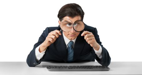 Businessman looking in a magnifying glass and working on a keyboard