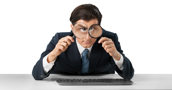 Businessman looking in a magnifying glass and working on a keyboard