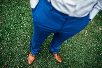 Stylish young man stands in lush green grass in a blue trousers