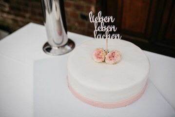 White cake topped with pink flowers and a sign in German 