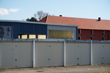 Obraz premium Reihe weißer alter Garagentore vor Fabrikhalle und rotem alten Backsteinhaus bei Sonne am Mittag im Frühling