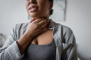 Cropped view of young multiracial woman touching sore throat at home.