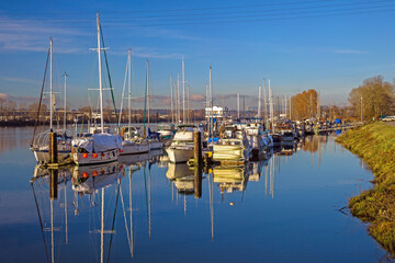 Fototapeta na wymiar Motor Boats and yachts in Marina and a reflection of a cloudy sky in water surface. This marina is located in the Steveston area of Richmond