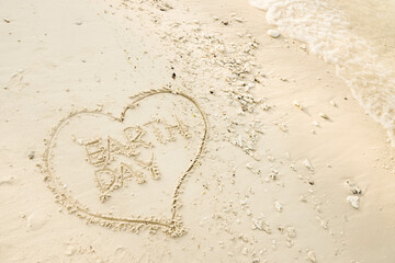 The word EARTH DAY is writting on the sand inside heart shaped sand writing with calm beach wave. drawing on the sand. writing with sands on the beach.