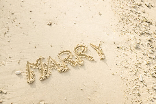 The word MARRY is writting on the sand. drawing on the sand. writing with sands on the beach.