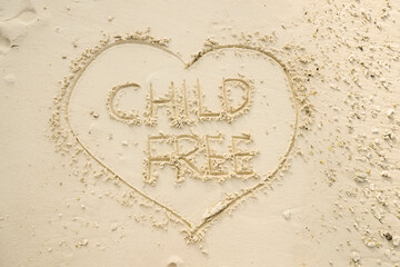 The word CHILD FREE is writting on the sand inside heart shaped sand writing. drawing on the sand. writing with sands on the beach.