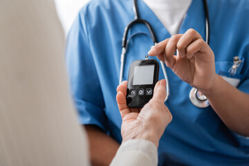 cropped view of multiracial nurse pointing with finger at glucometer with test strip near senior woman.
