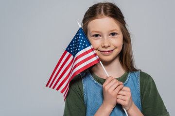 cheerful and patriotic girl holding flag of United States of America during memorial day isolated on grey.