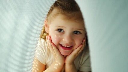 Little girl have a fun under blue knitted plaid in sunny morning