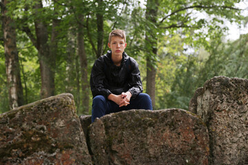 Naklejka na ściany i meble Portrait of a teenager boy sitting on large stones