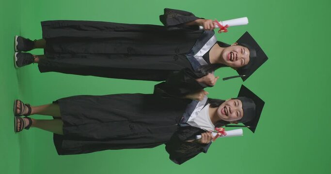 Full Body Of Asian Woman Students Graduate In Caps And Gowns Smiling And Showing Diplomas In Their Hands To Camera On The Green Screen Background In The Studio
