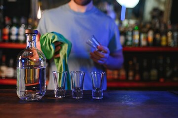 Barman pouring hard spirit into glasses for two male friends relaxing in a bar