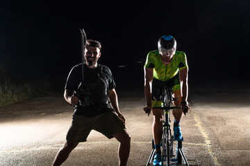 Behind the scenes. Professional videographer on a night shoot with a triathlete riding a bicycle...