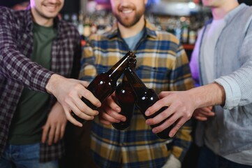 Young men in casual clothes are talking, laughing and drinking while sitting at bar counter in pub