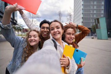 Smiling multiracial college students taking a selfie back to school. Happy friends photo together outside campus university holding folders. Cheerful classmates young people pose and amused.  - obrazy, fototapety, plakaty