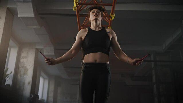 View from the botton to active sporty athletic woman, weightlifter exercising with skipping rope