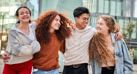 Portrait of group of four young students strolling happily around campus. Smiling friends and...