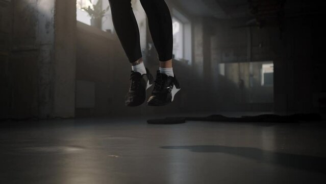 Close-up Legs of athletic woman weightlifter jumping with skipping rope in smokey gym. Slow motion