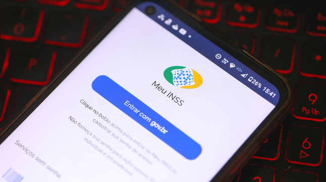 O aplicativo do INSS - Instituto Nacional do Seguro Social na tela de um telefone celular que est&aacute; sobre um teclado de laptop iluminado. Aposentadoria, Benef&iacute;cios, Brasil. 19/04/2023 - Brazil.