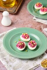 Boiled egg halves stuffed with beets, cream cheese and boiled yolks, sprinkled with pistachios on a green plate on a brown background. Egg snacks, stuffed eggs.