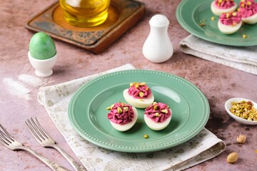 Boiled egg halves stuffed with beets, cream cheese and boiled yolks, sprinkled with pistachios on a green plate on a brown background. Egg snacks, stuffed eggs.