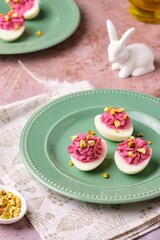 Boiled egg halves stuffed with beets, cream cheese and boiled yolks, sprinkled with pistachios on a green plate on a brown background. Egg snacks, stuffed eggs.