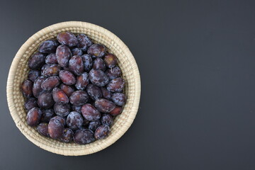 Fresh black dark plumes in wooden bowl on black background copy space vegan food homegrown products healthy fruits