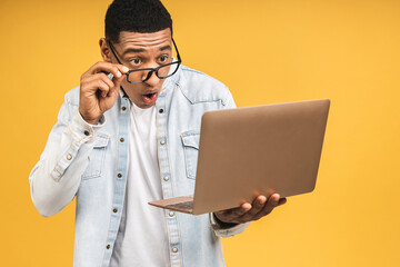 Young surprised shocked amazed african american man standing and using laptop computer isolated...