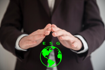 Świadomość biznesowa w zakresie ESG. Dłonie mężczyzny w marynarce przykrywające widok zielonej kuli ziemskiej z napisem ESG. - obrazy, fototapety, plakaty